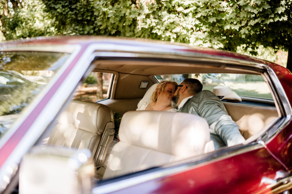 Brautpaar küsst sich in Brautauto. Fotograf fotografiert durch scheibe