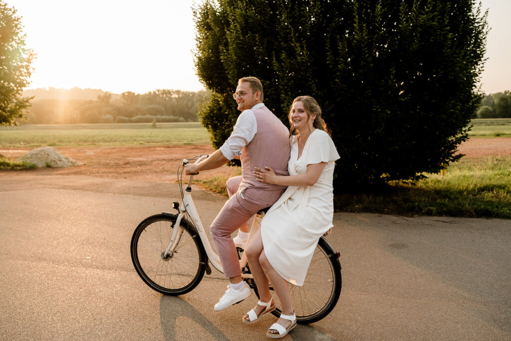 Brautpaar sitzt gemeinsam auf einem Fahrrad am Linslerhof, warmes Abendlicht