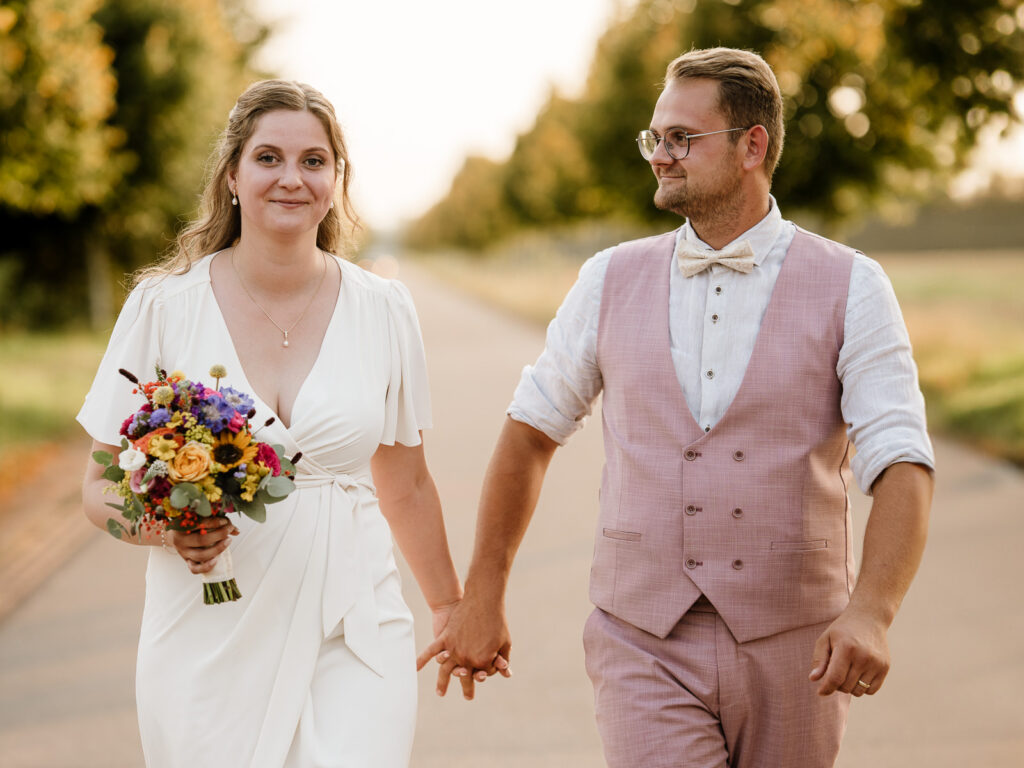 Brautpaar läuft in der Abendsonne auf Fotografin zu