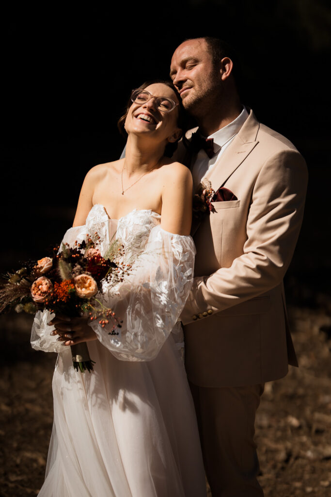 Bräutigam steht hinter Braut, Braut lacht. Foto entstand im harten Mittagslicht. Daher kontrastreich