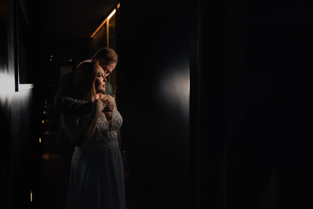 Brautpaar steht eng beieinander vor dunklem Hintergrund, nur Gesichter und Konturen im Licht sichtbar