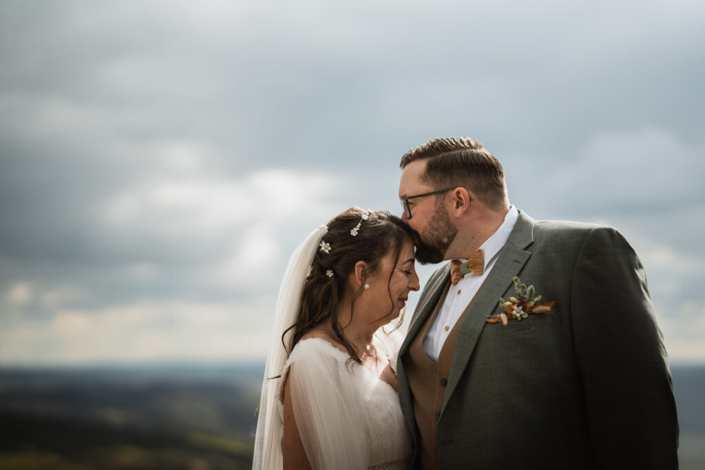 Bräutigam küsst Braut auf Stirn. Im Hintergrund weiter Horizont