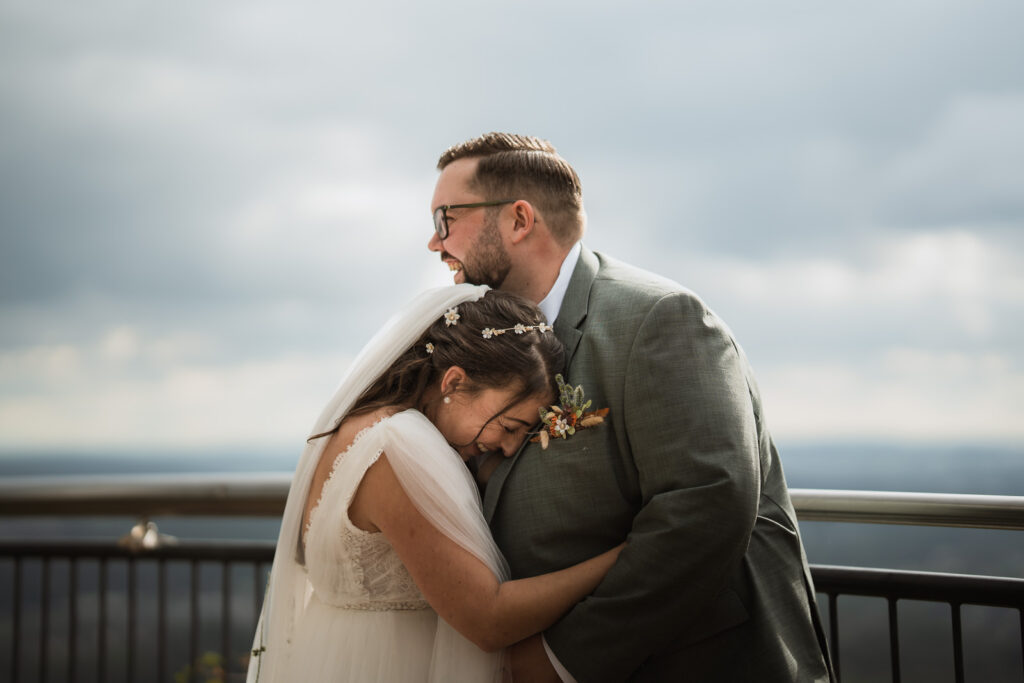 Braut lehnt sich an die Brust des Bräutigams und lacht, beide stehen sich gegenüber