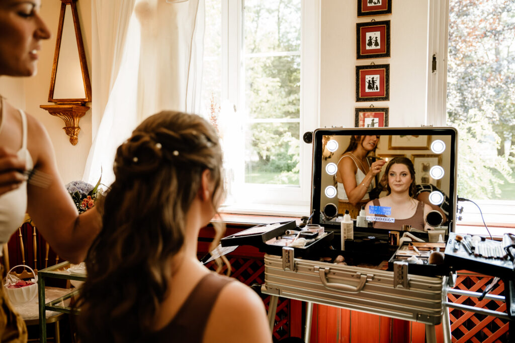 Braut sitzt im Zimmer und wird geschminkt