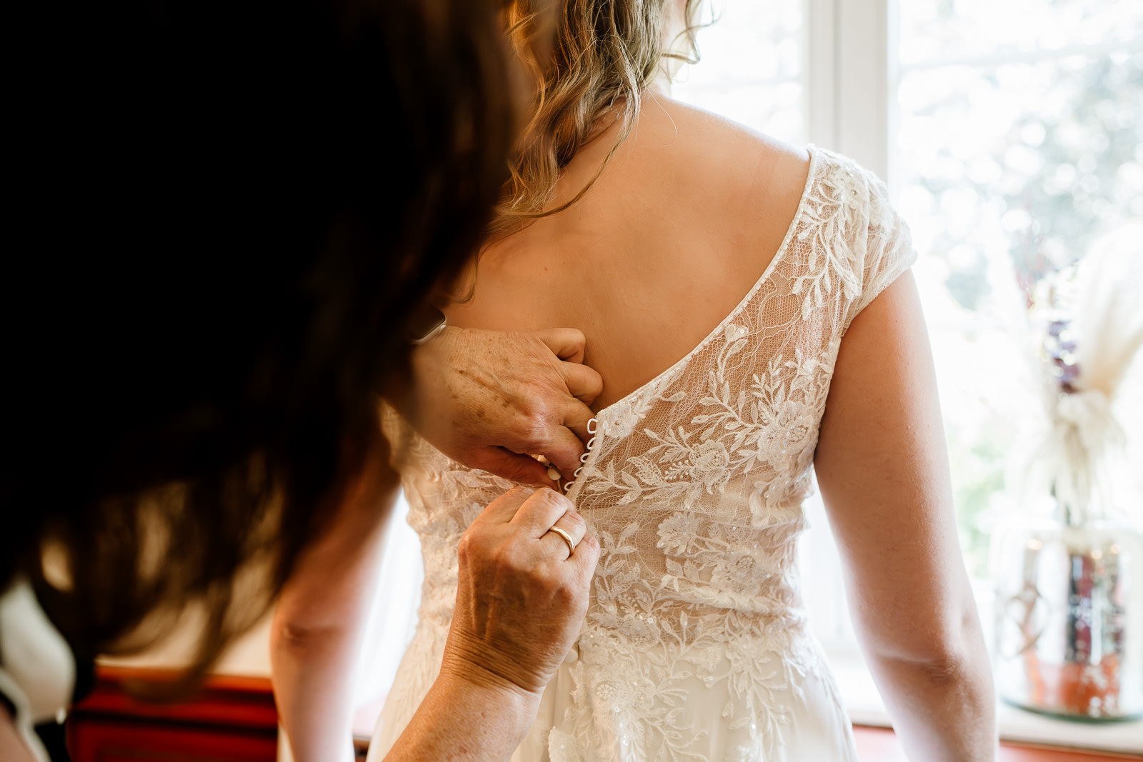 Frau knöpft Braut das Kleid am Rücken zu