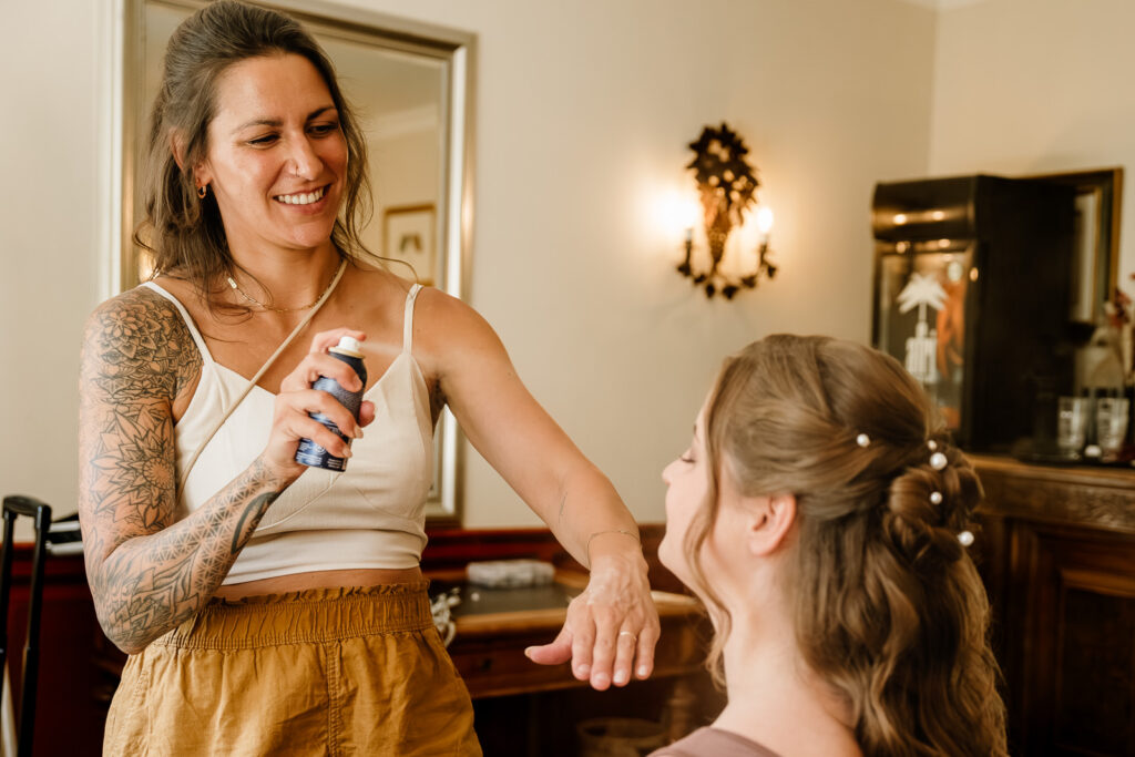 Stylistin sprüht Fixierspray auf geschminkte Frau