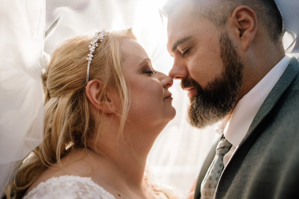 Nahaufnahme eines Brautpaares unter einem Schleier. Beide haben die Augen geschlossen