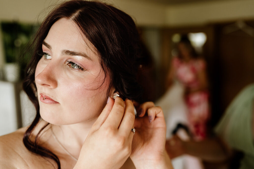 Braut steckt sich einen Ohrring an beim Brautstyling