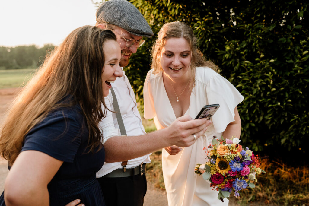Braut mit Gästen beim Lachen auf Hochzeit am Linsler Hof bei Sonnenuntergang