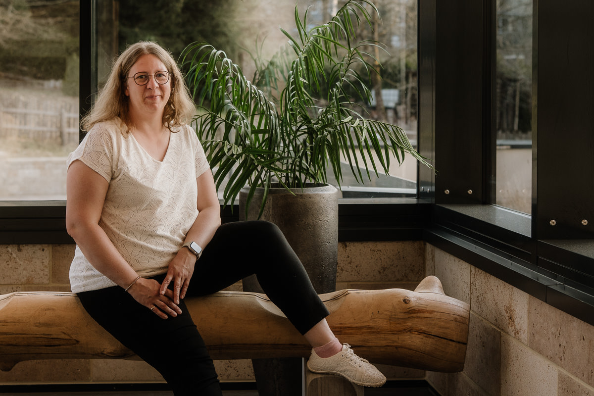 Hochzeitsfotografin Saskia aus dem Saarland sitzt entspannt auf Holzbank im Tageslicht