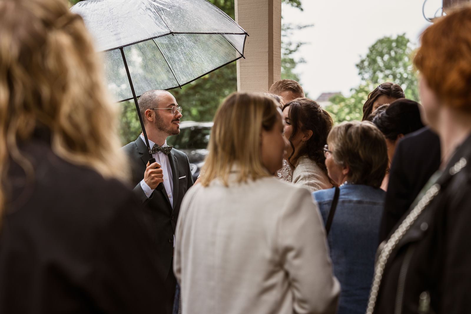 hochzeit bei regen mit Gästen unter einem Dach und Bräutigam mit Schirm