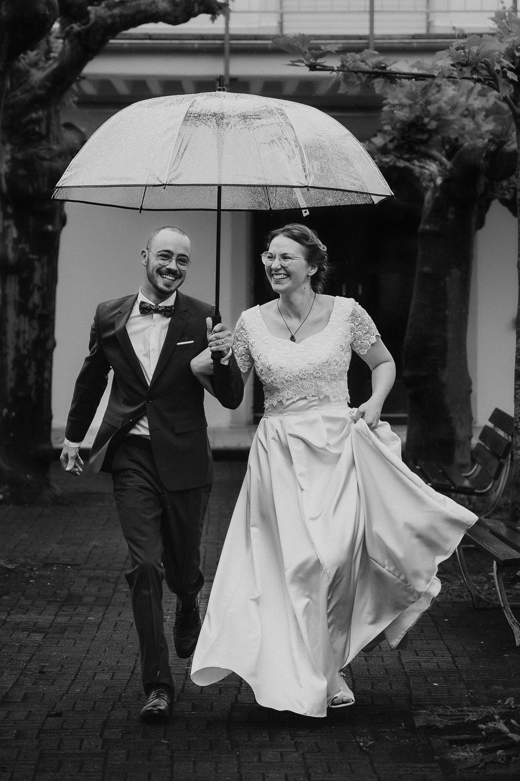 Regenhochzeit lachendes Brautpaar läuft zu Fotograf