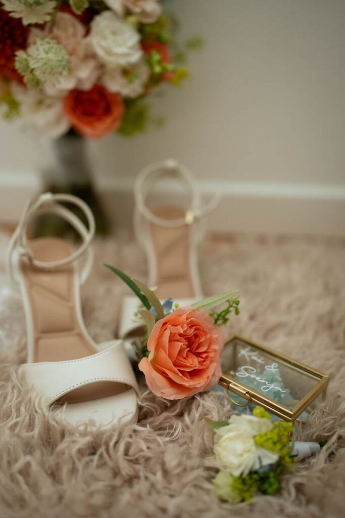 Brautschuhe, Blumen und Ringkästchen auf einem braunen Fell arrangiert