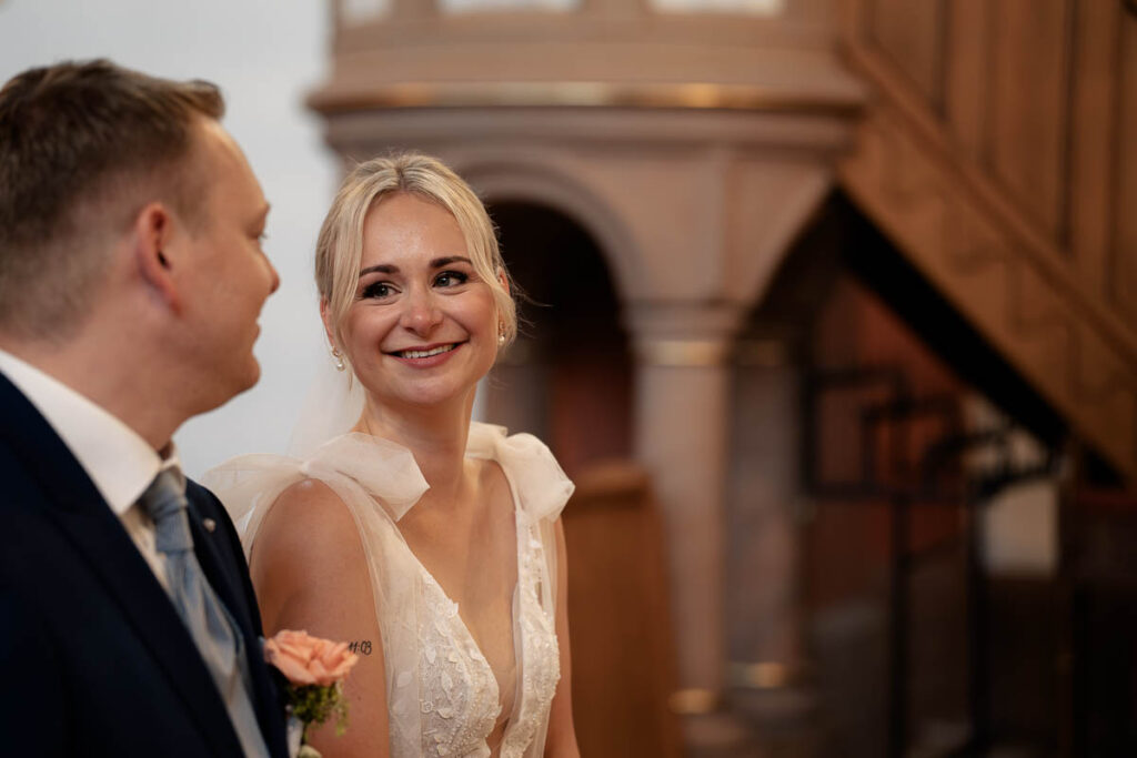 Braut strahlt ihren Bräutigam während einer kirchlichen Zeremonie der Hochzeit an